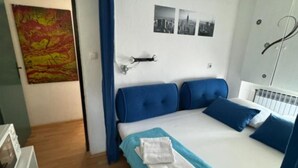 Een slaapkamer met een bed, blauwe hoofdborden, een witte radiator en een muur met drie zwart-wit foto's.