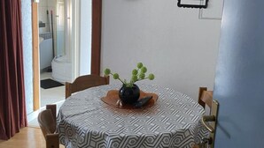 Un coin repas avec une table ronde recouverte d’une nappe à motifs, un vase avec des plantes vertes et une horloge au mur.