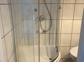 Eine begehbare, gläserne Dusche mit Handbrause und am Wand montiertem Wasserhahn.