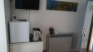 Una habitación con minibar blanco, televisor de pantalla plana en la pared, radiador y puerta.