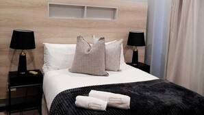 Une chambre d’hôtel comprenant un lit, deux tables de chevet avec des lampes, une tête de lit, un appareil de climatisation et une fenêtre avec des rideaux.