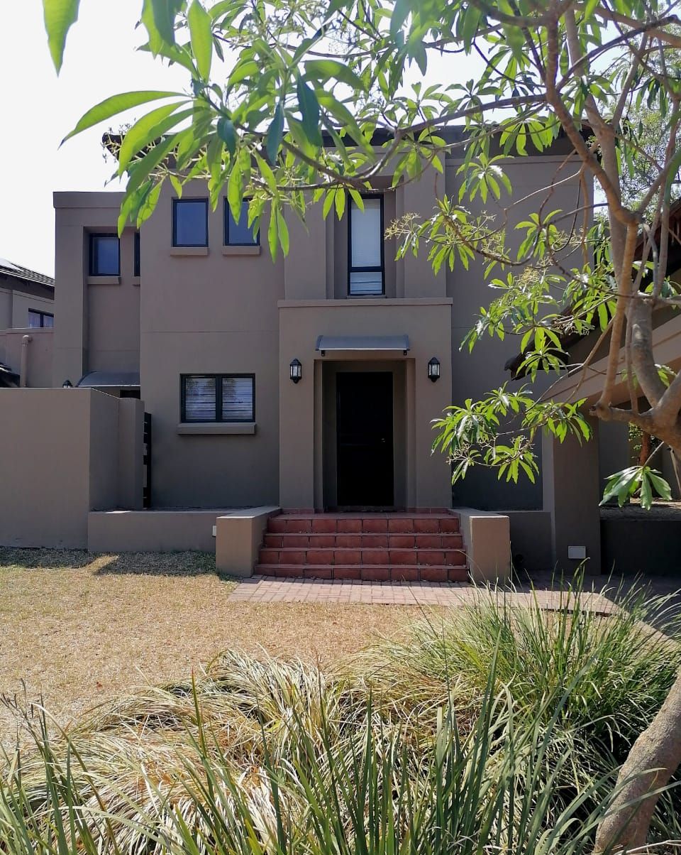 A modern building with a flat facade, a central entrance with steps, and a small garden area with grass and a tree.