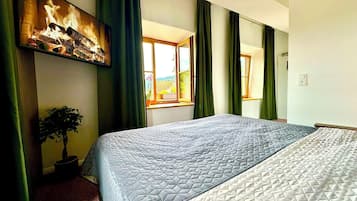 Ein Hotelzimmer mit einem großen Bett, einem Bild an der Wand, einer Zimmerpflanze und einem Fenster mit Vorhängen.