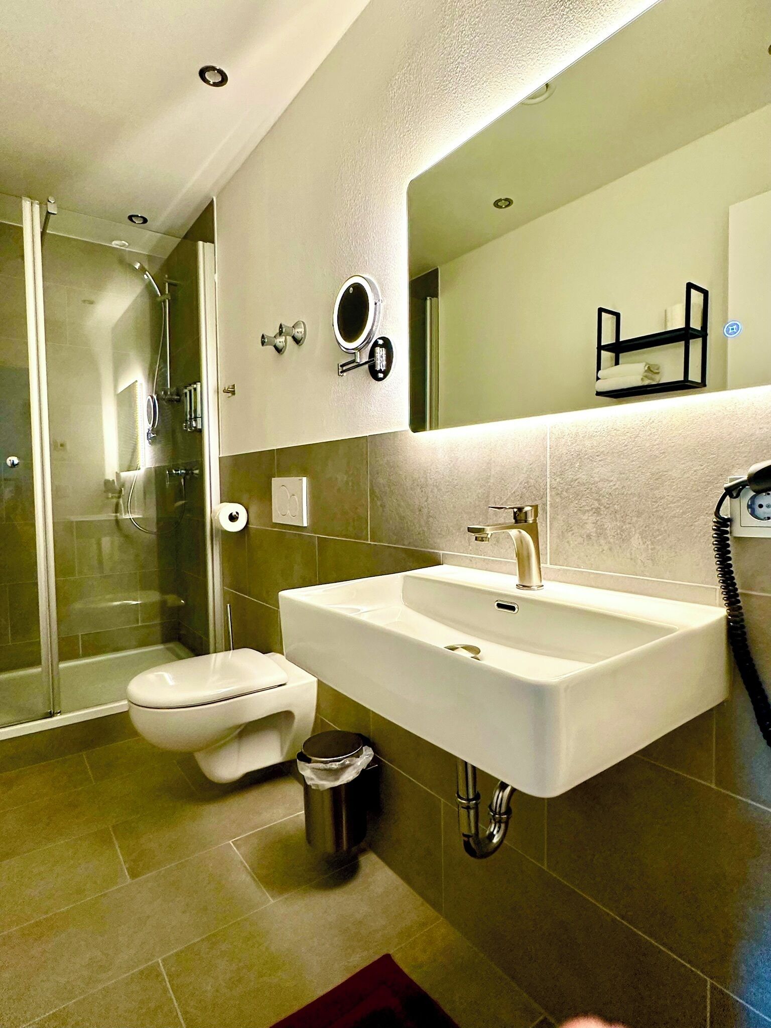 A modern bathroom with a glass-enclosed shower, a white sink with a mirror above it, and a toilet.