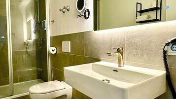 A modern bathroom with a glass-enclosed shower, a white sink with a mirror above it, and a toilet.