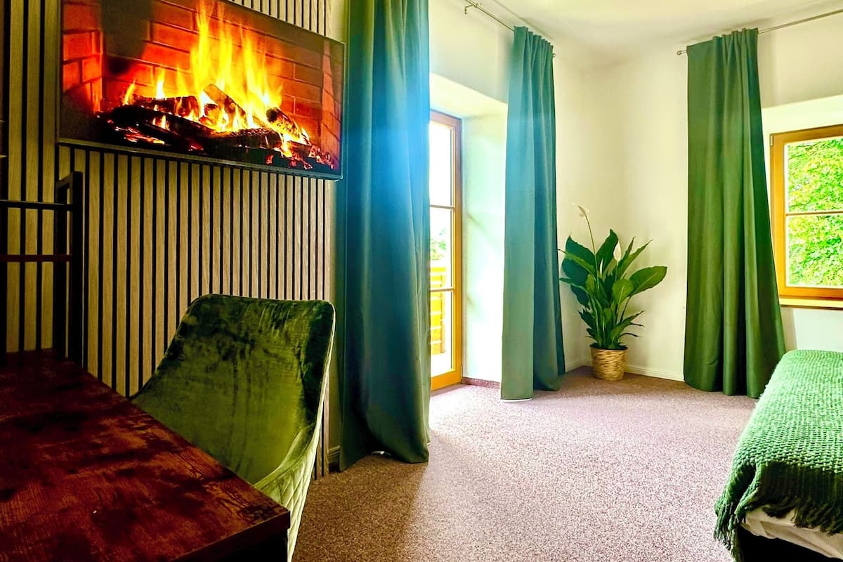 A room with a fireplace, green curtains, a plant, and a bed.