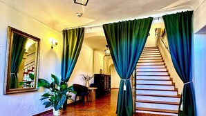 A hallway with a staircase, green curtains, a potted plant, a mirror, and a lamp. - Hotel Bergen Zur Post by Rikas Hotels (Bergen)