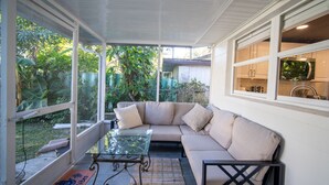 Un patio cubierto con una mesa de vidrio, sofá color crema y vista a follaje.