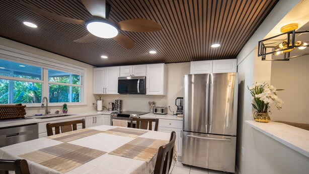Una cocina moderna con armarios blancos, electrodomésticos de acero inoxidable y un comedor con una mesa preparada para cuatro.