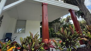 Una casa con porche cubierto sostenido por pilares rojos, rodeada de diversas plantas y árboles.