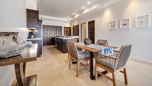 A modern kitchen with a dining area, featuring a large island, dark cabinetry, and a tiled floor.