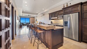 A modern kitchen with a central island, bar stools, stainless steel appliances, and dark wood cabinetry.