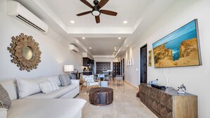 A spacious living area with a modern sofa, a wooden coffee table, and a large painting of a coastal landscape.