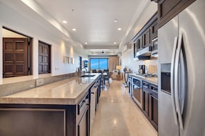 A modern kitchen with a large island, stainless steel appliances, and a view to the living area. - CCV Quivira - New charming 2BR w/ Ocean view & Golf Access! (Cabo San Lucas)