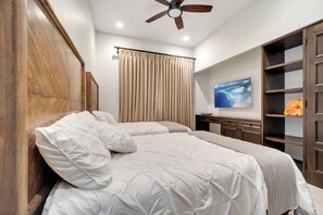 Een slaapkamer met een bed, een plafondventilator, een televisie en een houten garderobe.