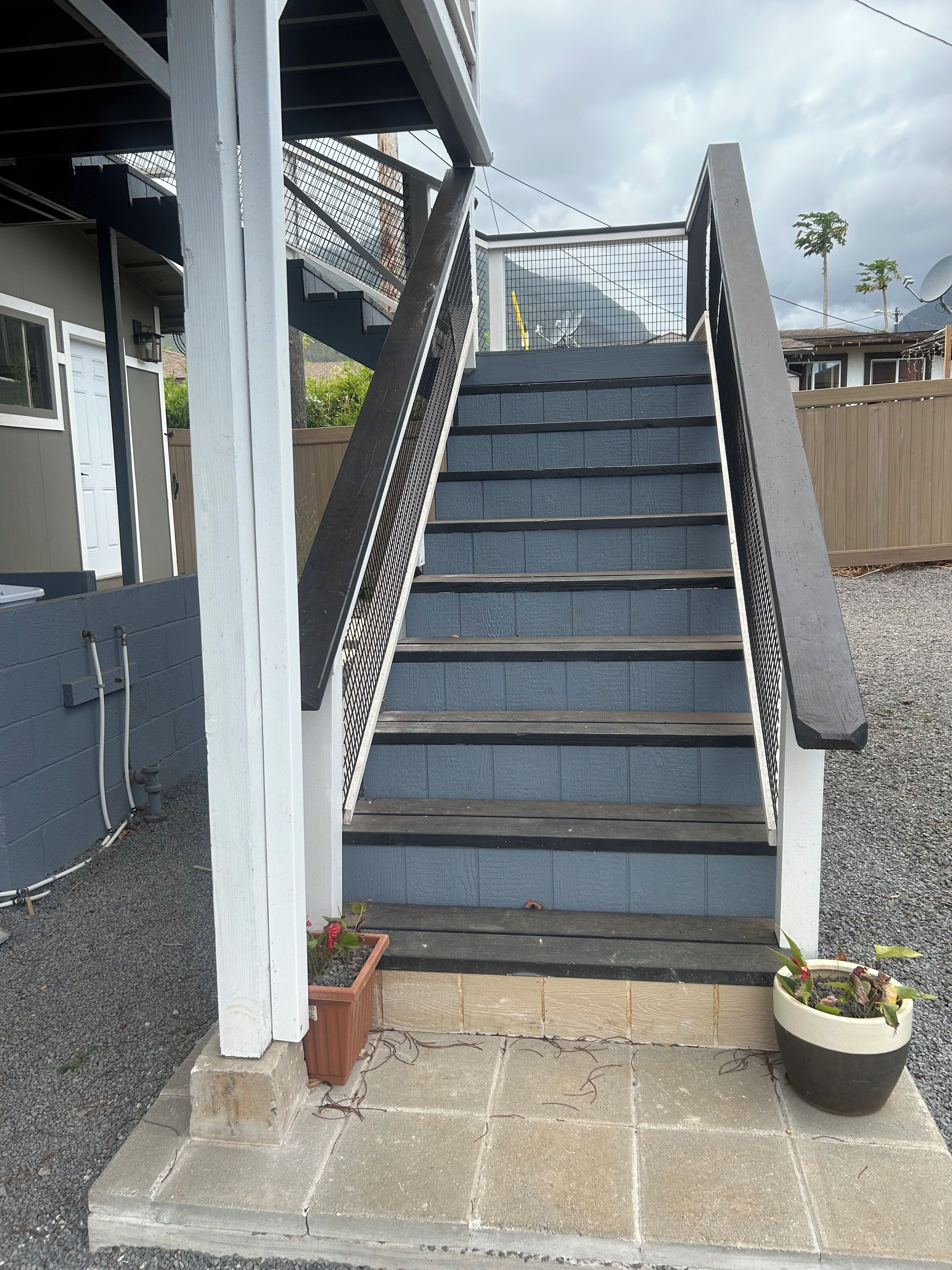 Eine Treppe führt zu einer überdachten Veranda mit einem Metallgeländer, einem Holzzaun und Blumentöpfen am Fuß.