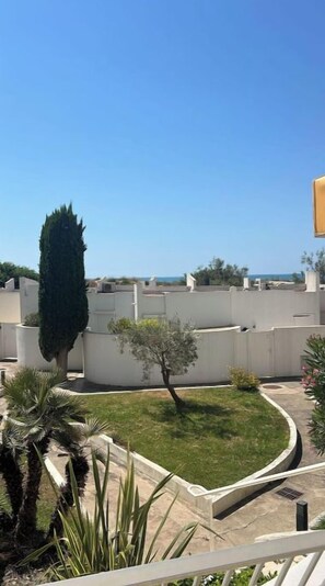Un jardin sur le toit, avec un palmier, un petit arbre et un ciel bleu dégagé.