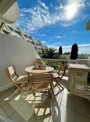 Un balcon avec une table ronde et des chaises, un meuble, et une vue sur des palmiers et des immeubles.