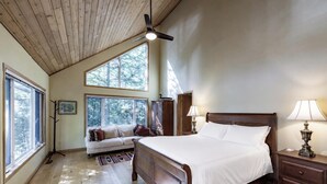 A bedroom with a large bed, a ceiling fan, a nightstand, a lamp, a dresser, a window, and a sofa.