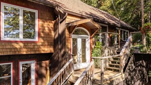 A wooden house with a front porch, a staircase leading to the entrance, and a large window.