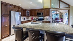 A modern kitchen with dark wood cabinets, stainless steel appliances, a granite countertop, and a bar area with leather chairs.