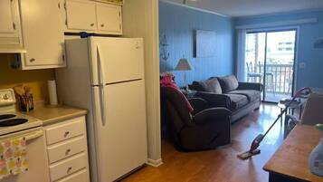 Una cocina compacta con refrigerador, estufa y armarios. Hay un comedor con mesa y sillas, y una sala de estar con sofá y ventana.