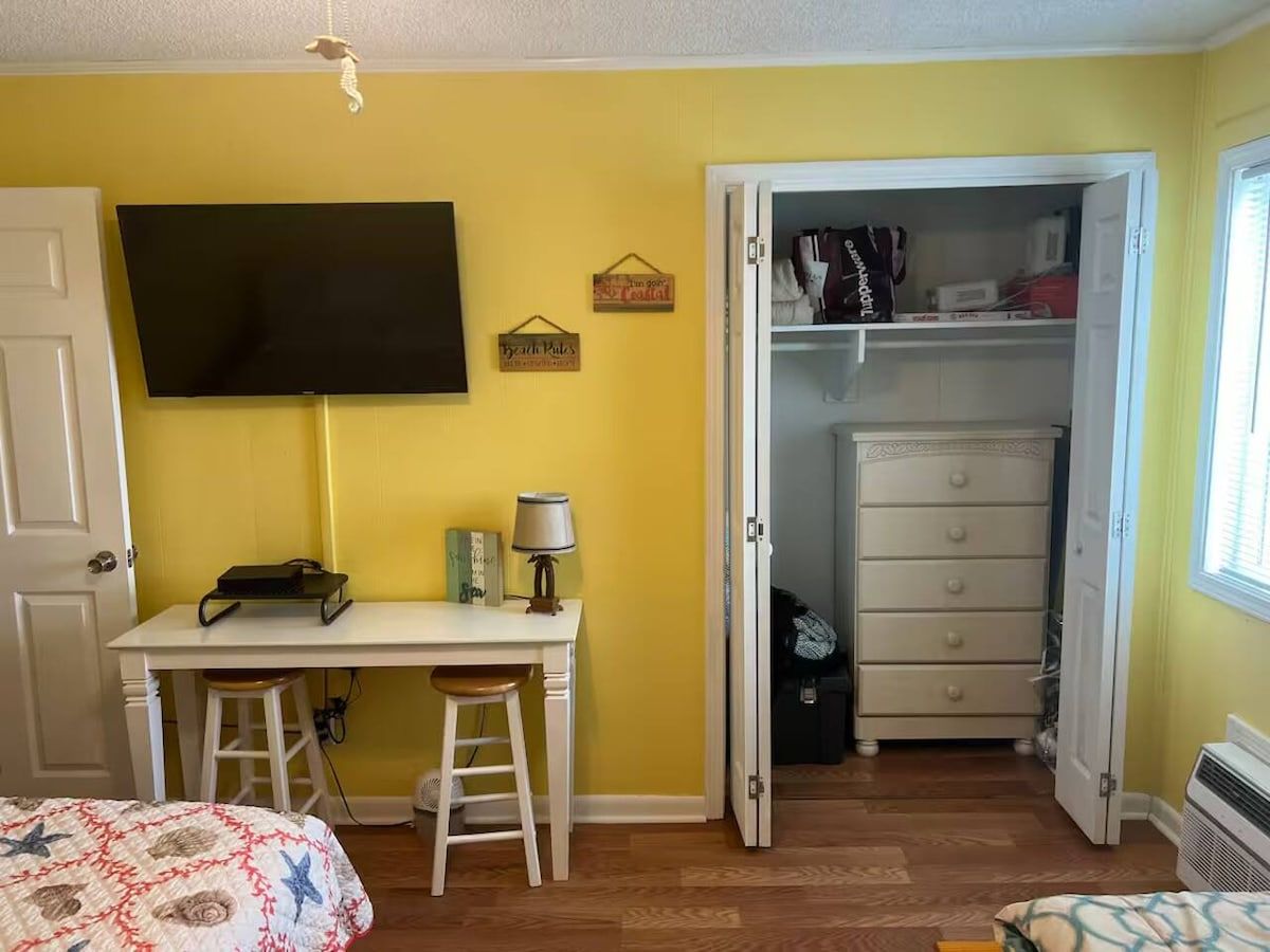 Een slaapkamer met een bed, een bureau, een stoel, een televisie, een kast en een deur.