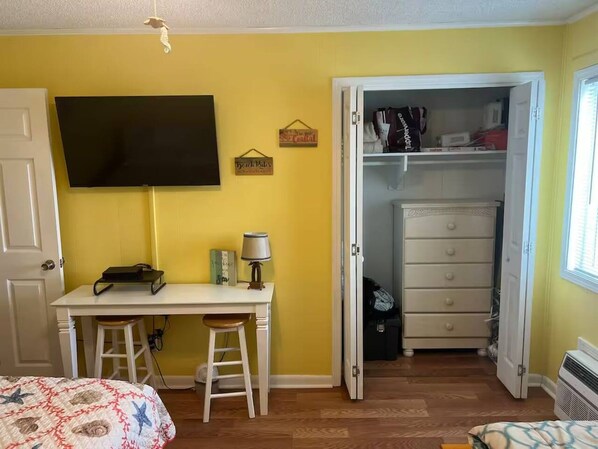 Un dormitorio con cama, escritorio, silla, televisor, armario y puerta.
