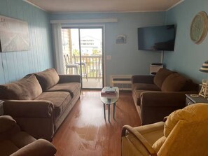 A living room with a brown sofa set, a small round table, and a television on the wall.