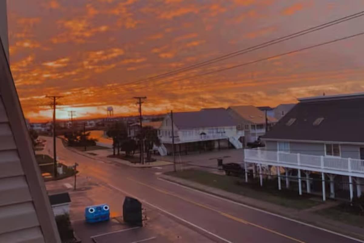 Une rue résidentielle bordée de maisons, avec une route et un ciel au coucher du soleil.