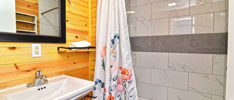 Un baño con pared de madera, un lavamanos blanco, un espejo y una cortina de ducha con motivos florales.