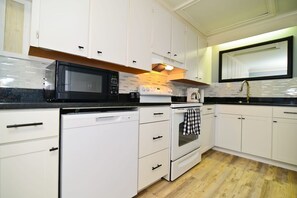 Una cocina moderna con armarios blancos, un microondas negro, una estufa y un lavavajillas.