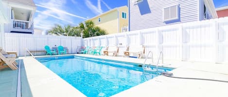 En swimmingpool med ett vitt staket, ett trädäck och ett litet hus med en balkong.