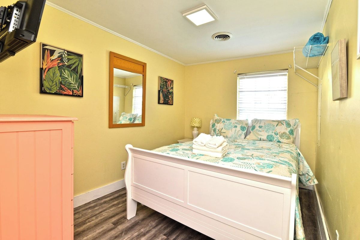 Un dormitorio con cama, cómoda, ventana y dos cuadros colgados en la pared.