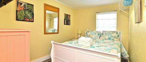 Un dormitorio con cama, cómoda, ventana y dos cuadros colgados en la pared.