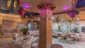 Un espace extérieur aménagé en terrasse, avec des meubles en bois, des plantes suspendues et un sol carrelé.