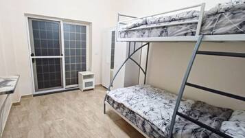 A dormitory room with bunk beds, a sliding glass door, a small table, and a window.