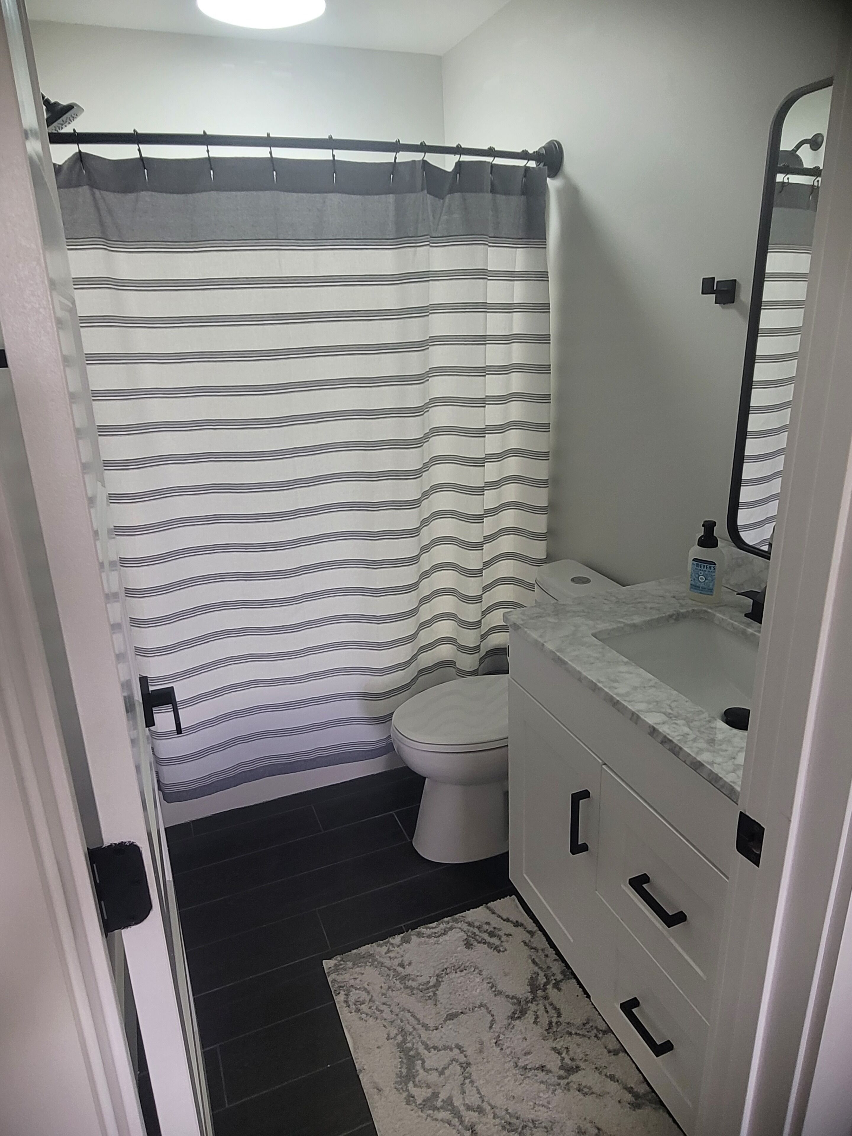 Ein Badezimmer mit gestreifter Duschvorhang, Toilette, Waschbecken mit Marmorplatte und Spiegel.