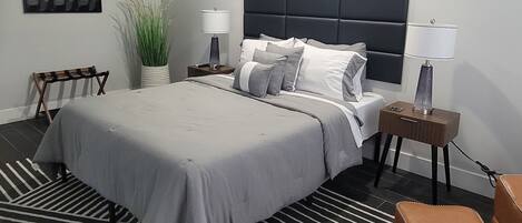 A modern bedroom with a large bed, a headboard, bedside tables, a bench, and a potted plant.