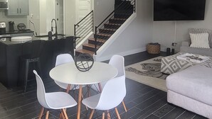 A modern living space with a dining area, kitchen, staircase, and a flat-screen TV.
