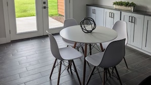 A modern kitchen with a round dining table, white cabinets, and a large wall clock.