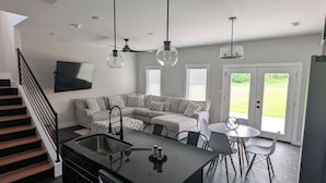 A modern kitchen with a central island, a dining area with a round table, and a living area with a sofa and TV.