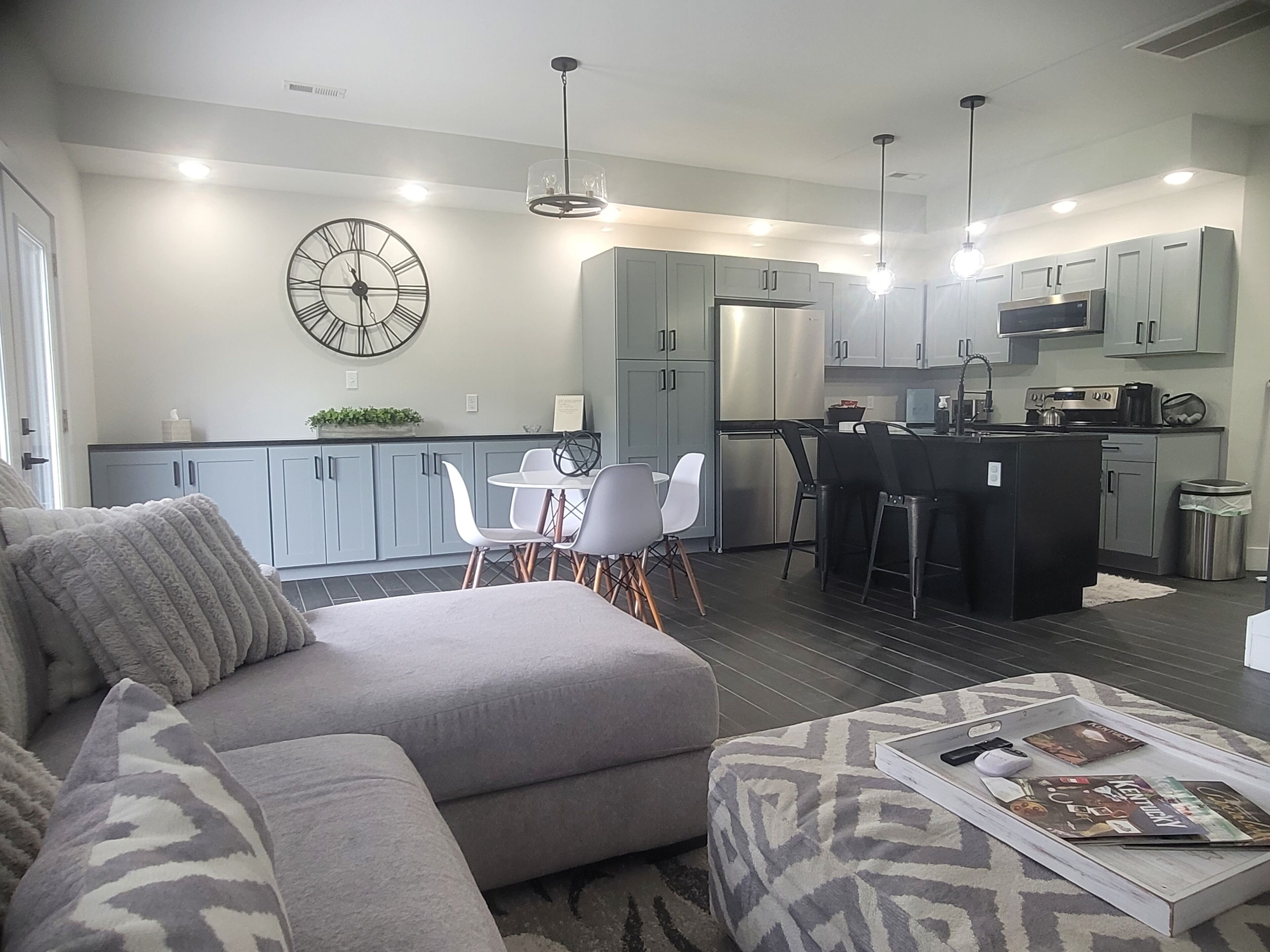A modern kitchen with grey cabinets, a central island, and a dining area with chairs.