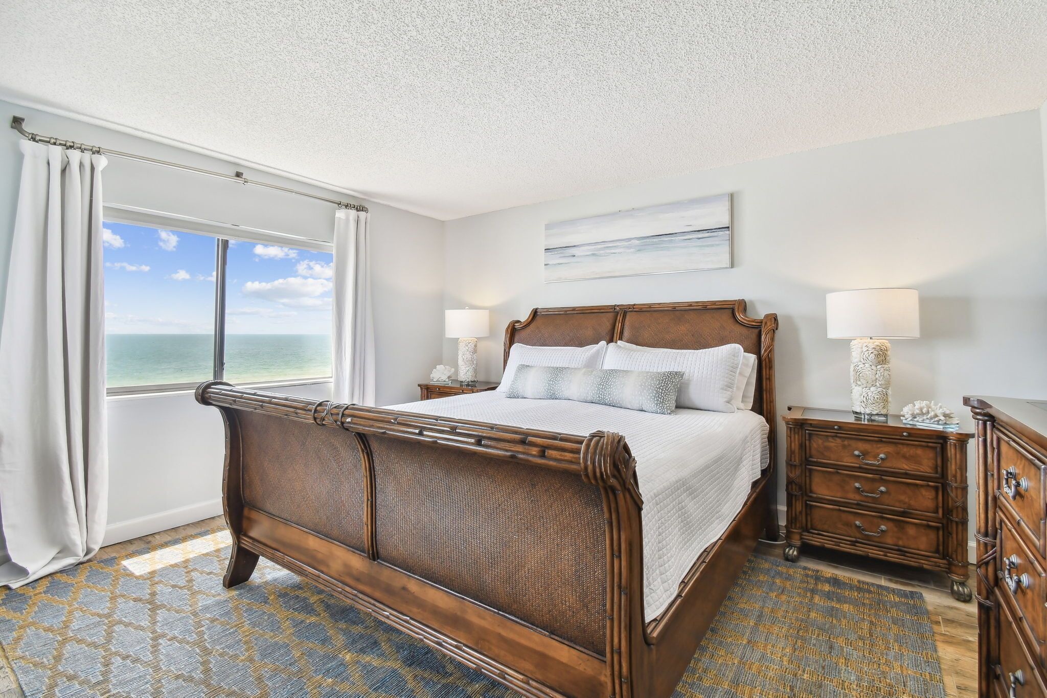 A bedroom with a large bed, a view of the ocean, and a wooden dresser.