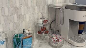 Una encimera de cocina con cafetera, licuadora, tarro de mezcla de café y un recipiente con bolsitas de té.