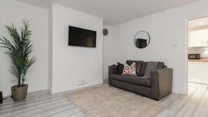 Una sala de estar moderna con un sofá gris, un televisor de pantalla plana, un espejo redondo y una planta en maceta.