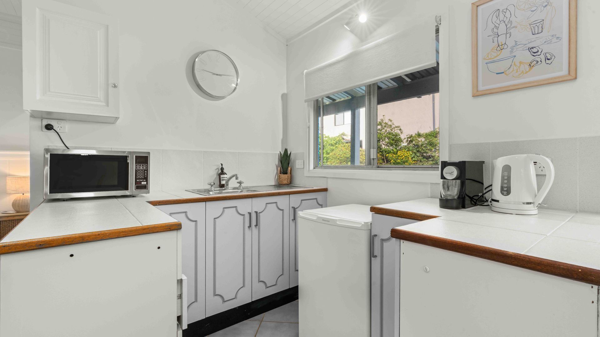Une cuisine moderne avec des meubles blancs, un four à micro-ondes, une machine à café et une fenêtre donnant sur un paysage verdoyant.