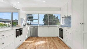 Cucina moderna con mobili bianchi, lavastoviglie in acciaio inossidabile e un'ampia finestra vista mare.