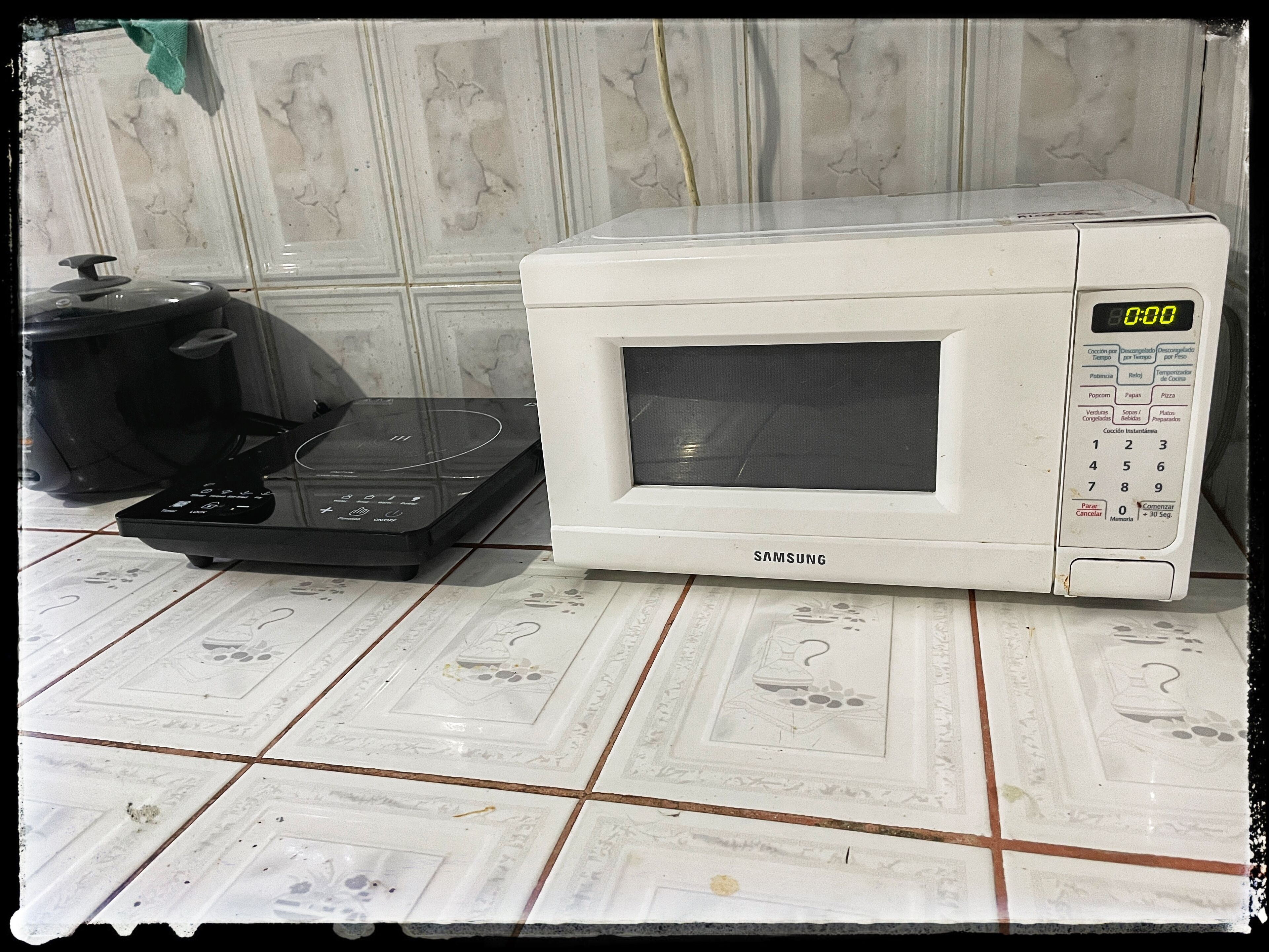 A white microwave oven with a digital display and a control panel, placed on a tiled kitchen counter.