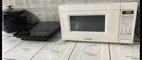 A white microwave oven with a digital display and a control panel, placed on a tiled kitchen counter.